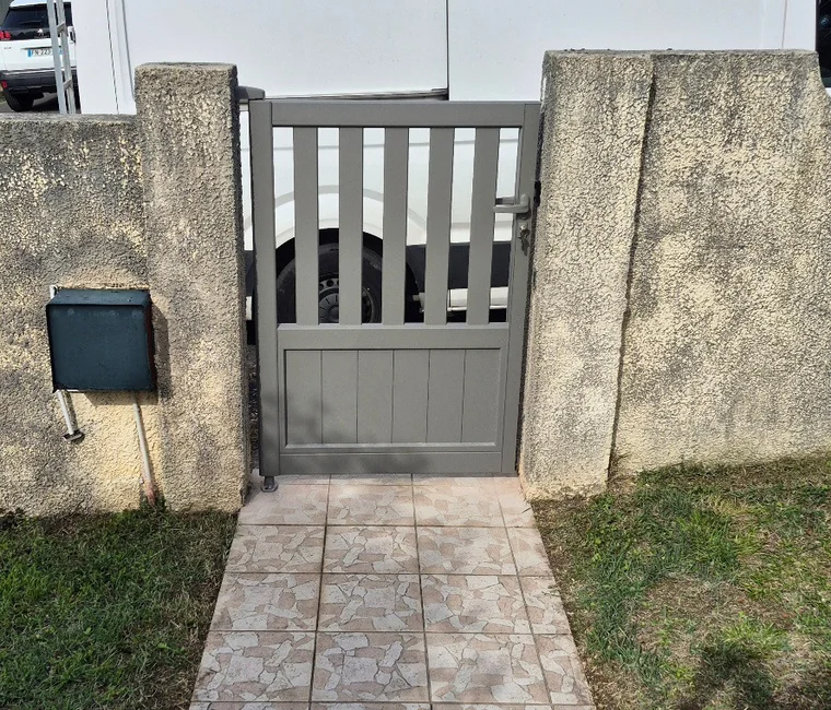 Portillon gris ajouré entre deux piliers maçonnés