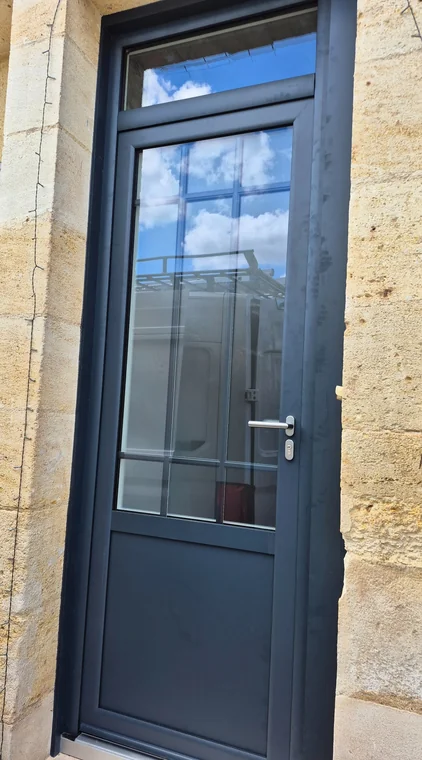Porte vitrée anthracite et imposte dans un encadrement en pierre